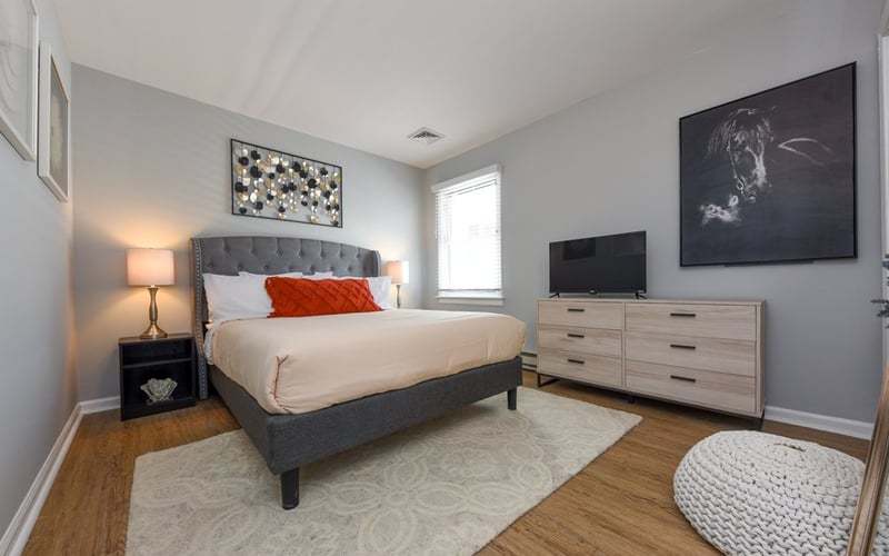 Grey bedroom with tufted headboard and orange accent pillow